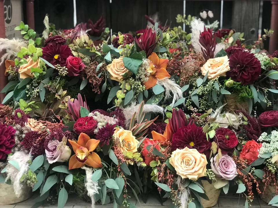 Long autumn table arrangement with orchids, roses, greenery, burgundy, peach, and cream flowers.