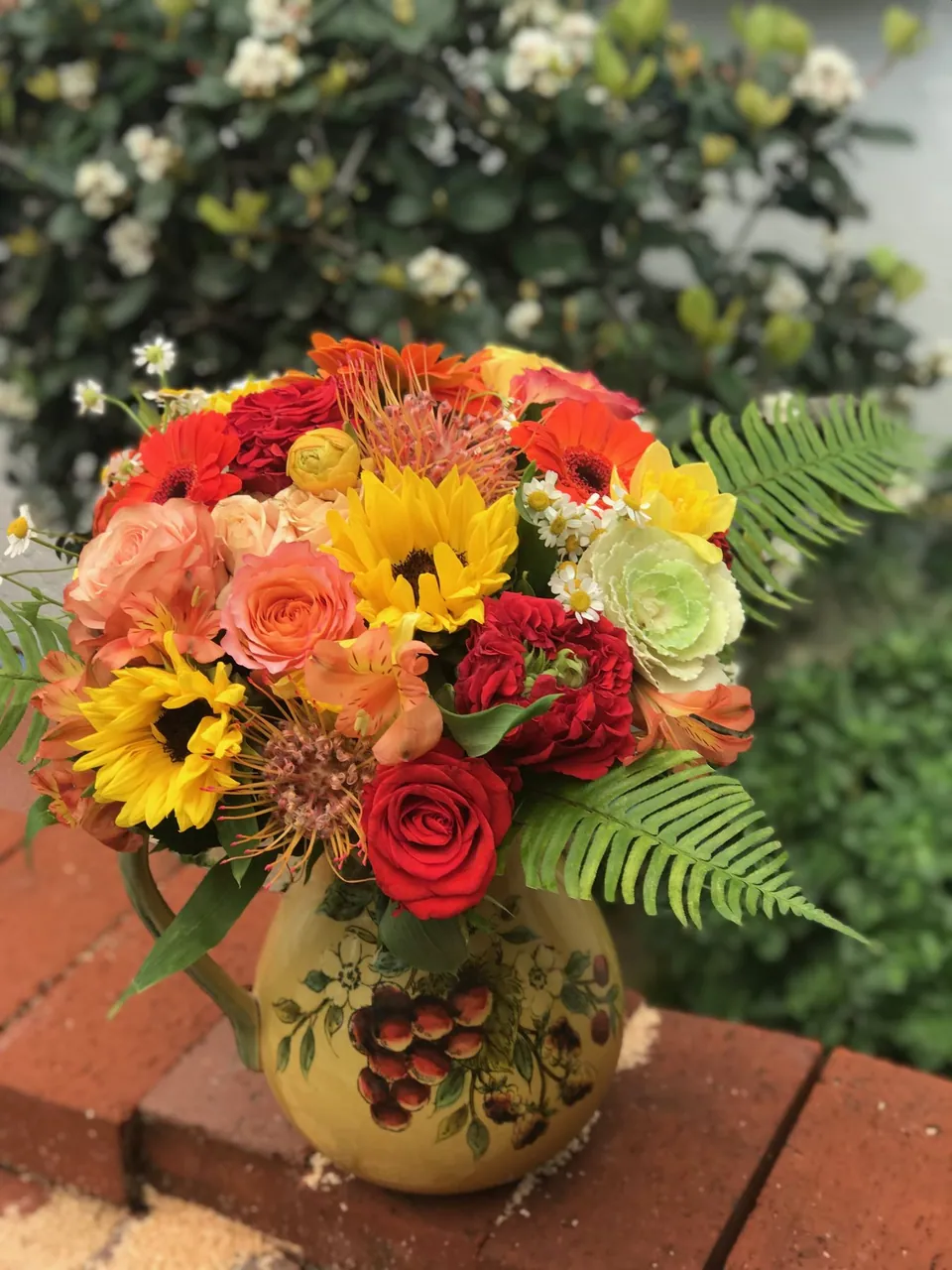 Bright yellow pitcher arrangement with sunflowers, red, orange, and green seasonal flowers.