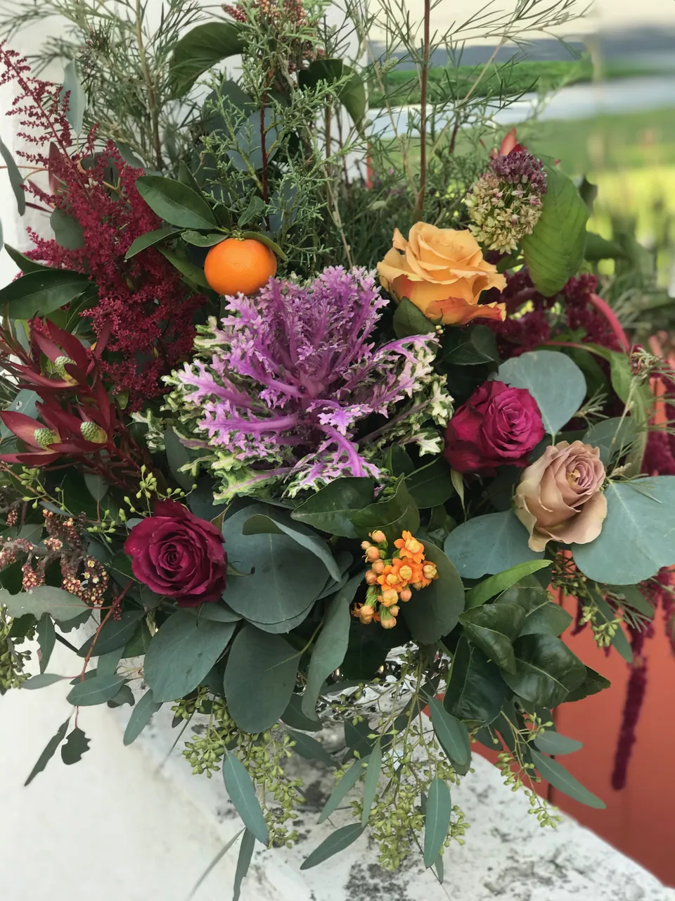 Garden arrangement with citrus, roses, burgundy flowers, and textured foliage.