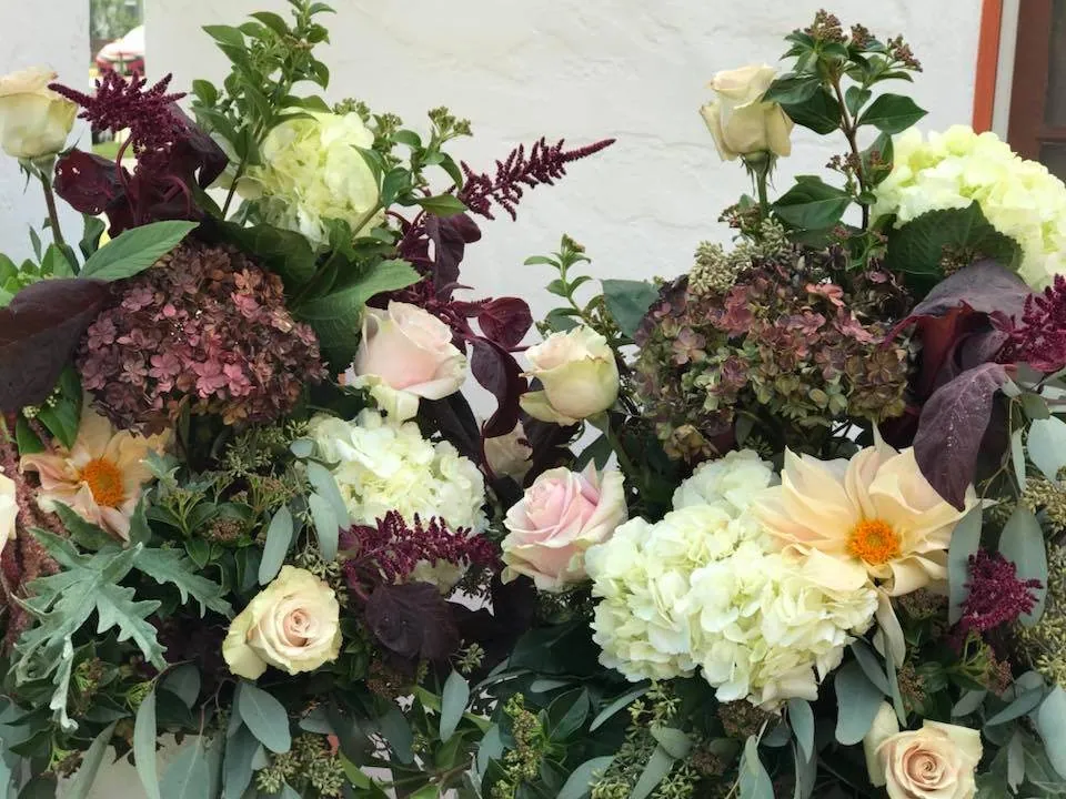 Garden bouquet with cream roses, burgundy accents, and loose greenery.
