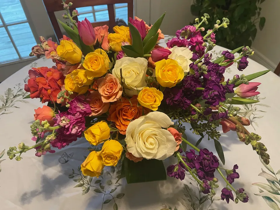 Low centerpiece with yellow roses, burgundy and purple flowers, tulips, and greenery.