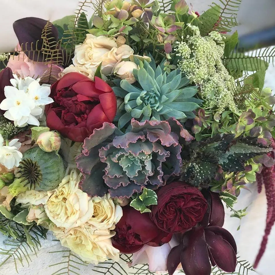Moody bouquet with burgundy roses, succulents, and cream flowers.