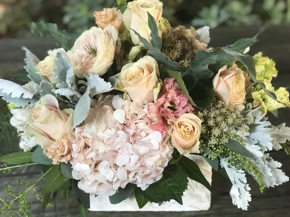 Pale pink, cream, and dusty green arrangement with soft roses and textured filler.