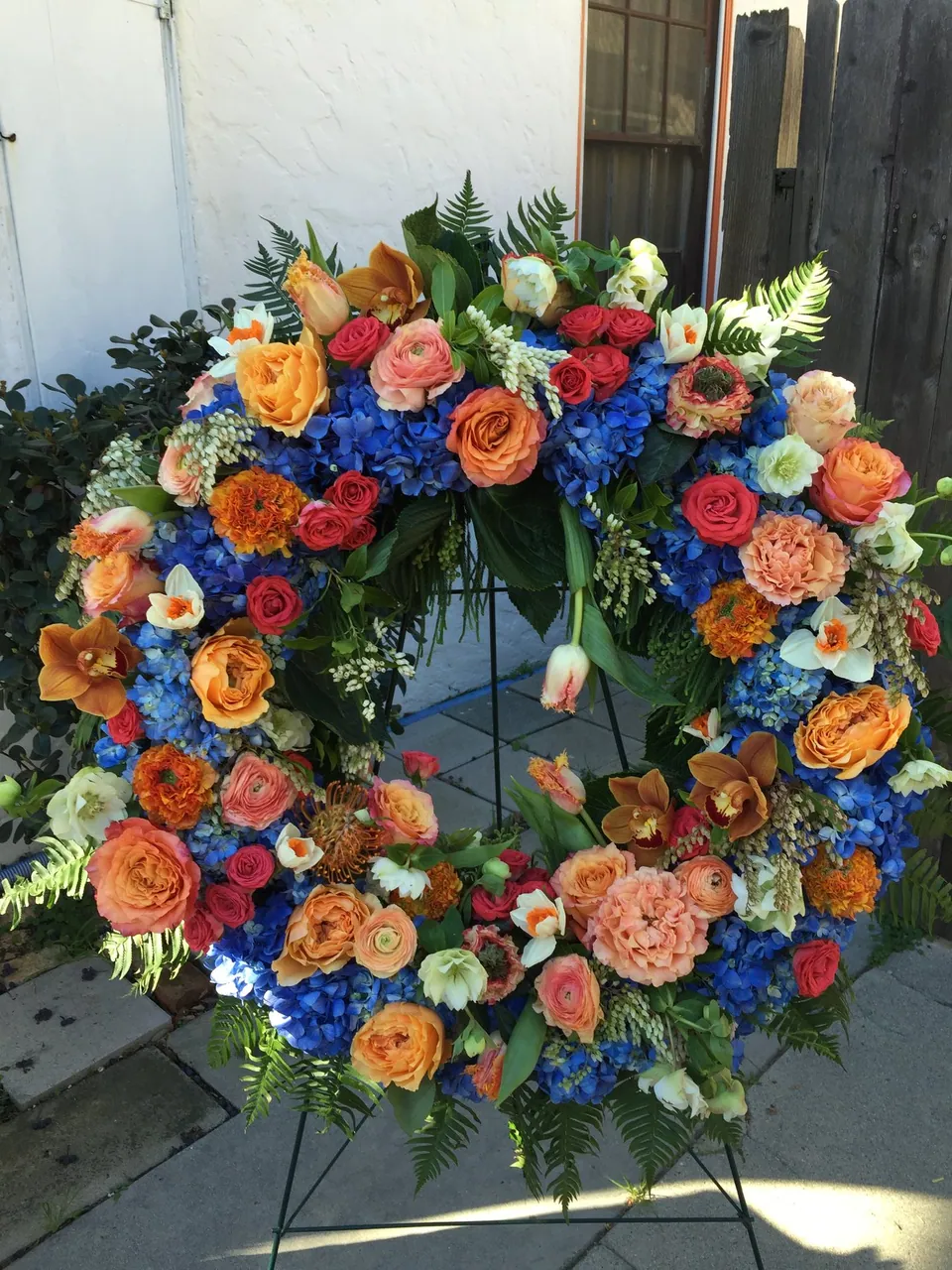 Round floral wreath covered in orange, blue, yellow, and pink flowers.