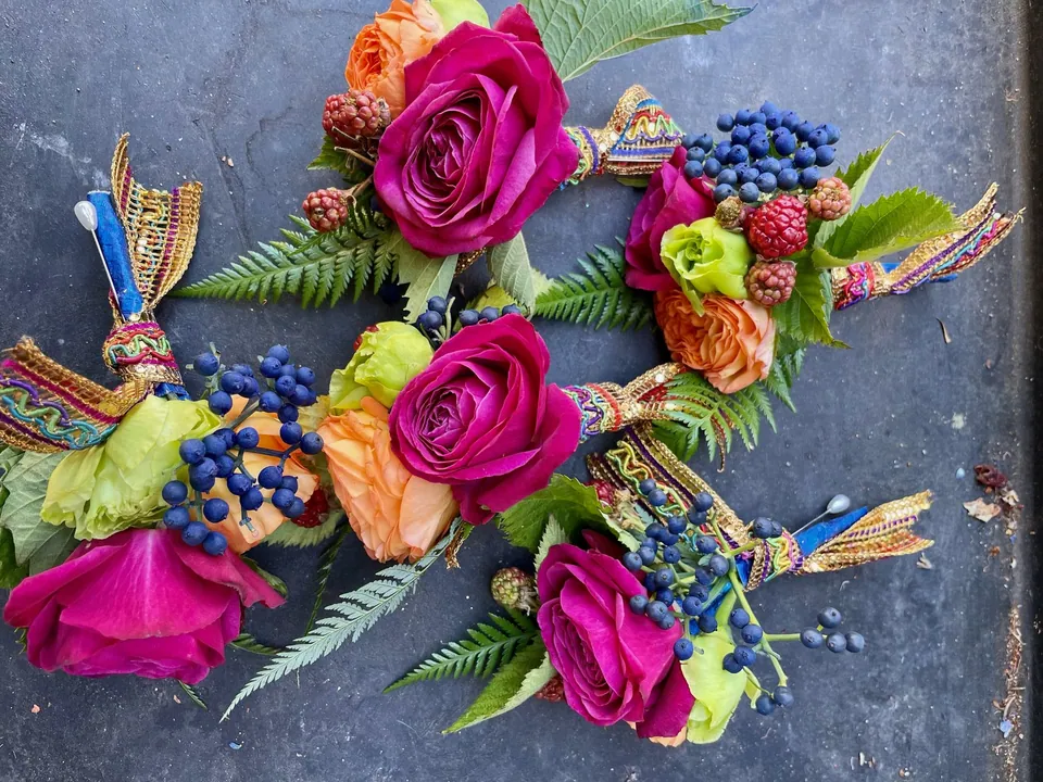 Small floral wearables with magenta roses, blue berries, wheat, and colorful ribbon.