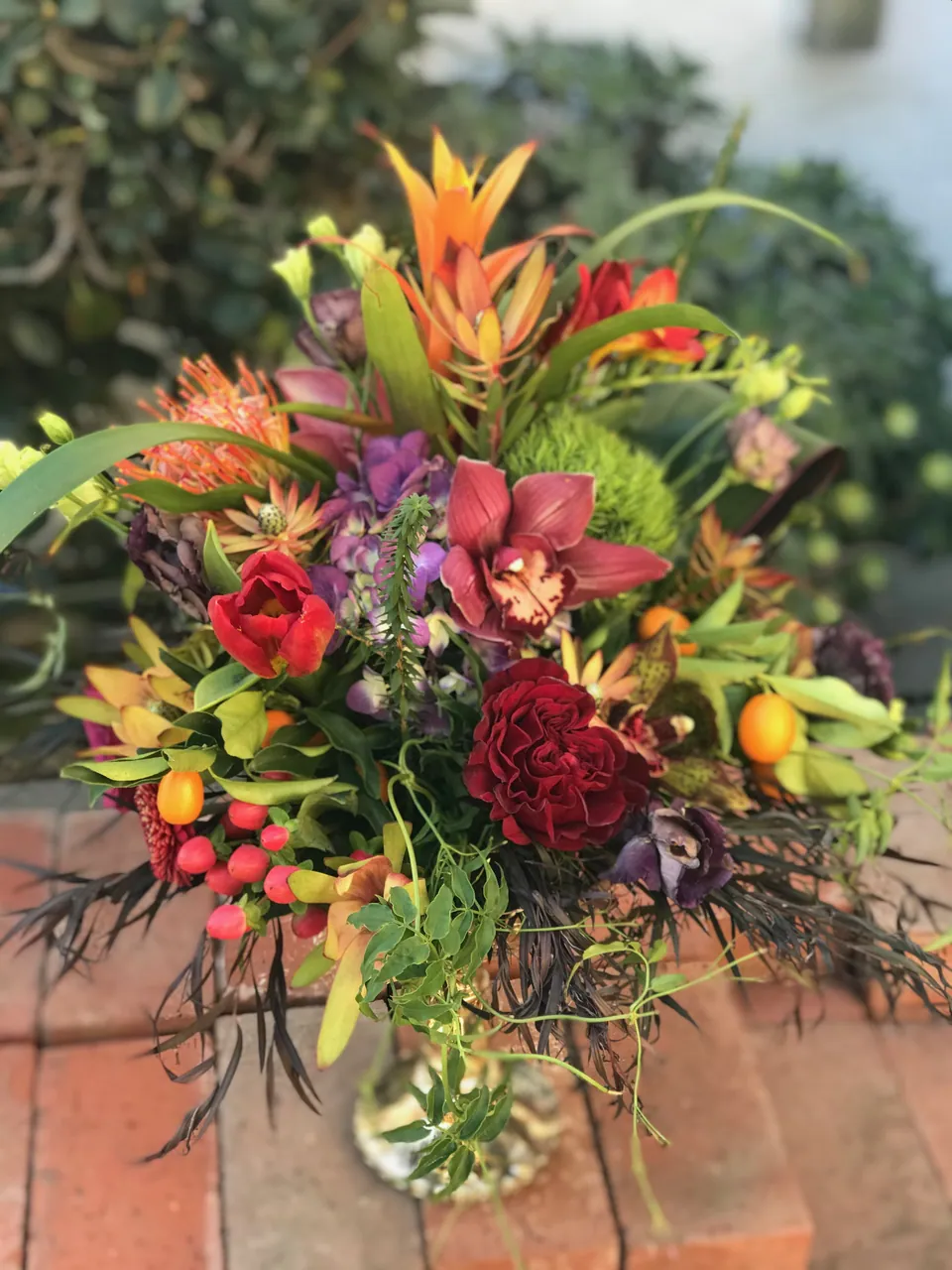 Tall sculptural floral arrangement with citrus, berries, roses, tropical leaves, and vivid garden color.