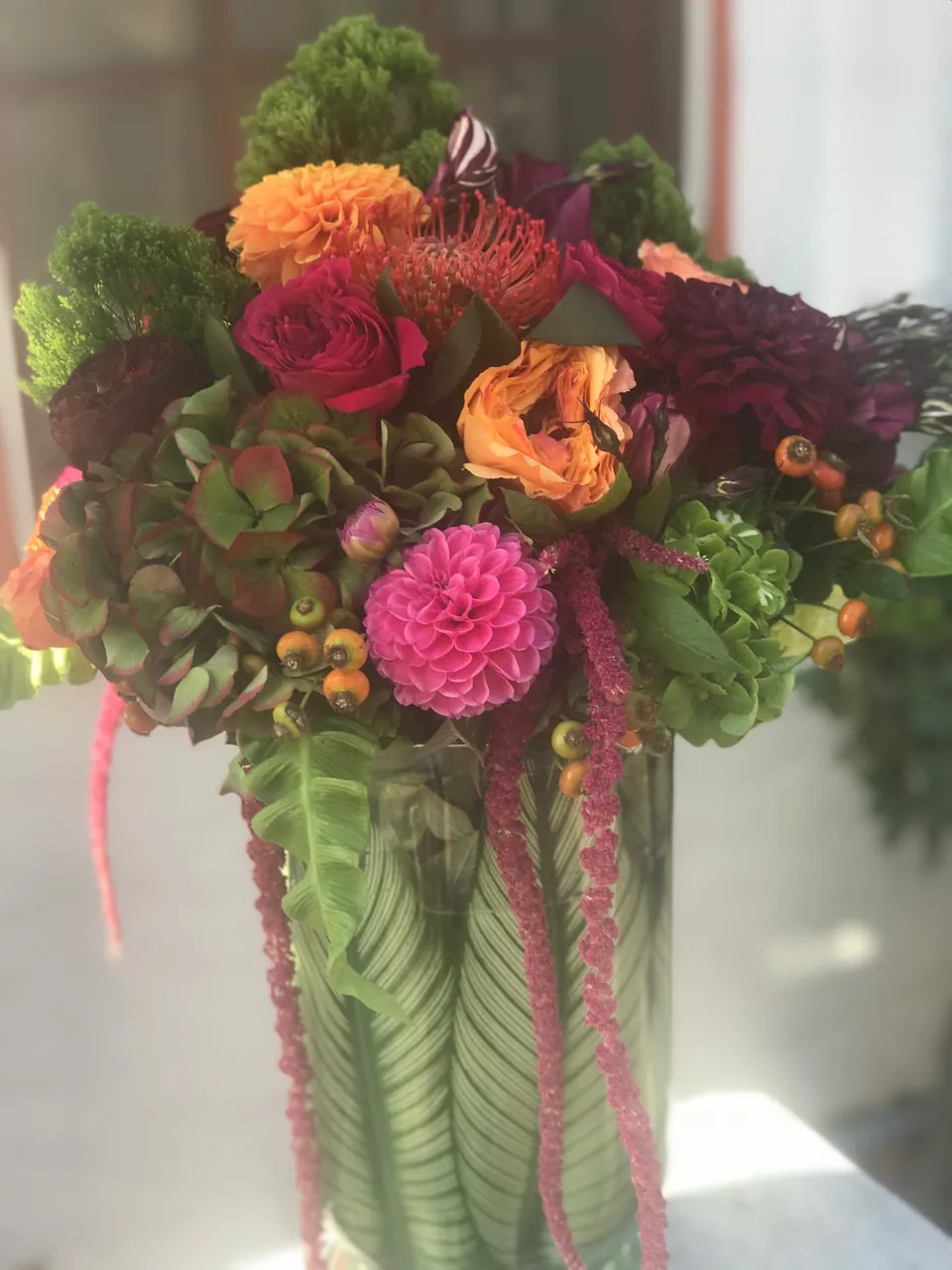 Tall sculptural floral arrangement with magenta, orange, green, and striped vessel.