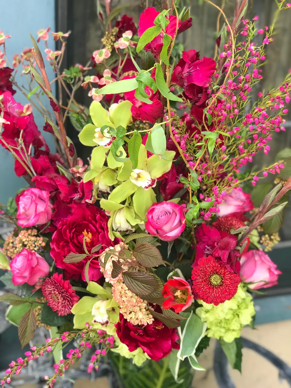 Tall vivid floral arrangement with orchids, roses, chartreuse accents, and architectural line.