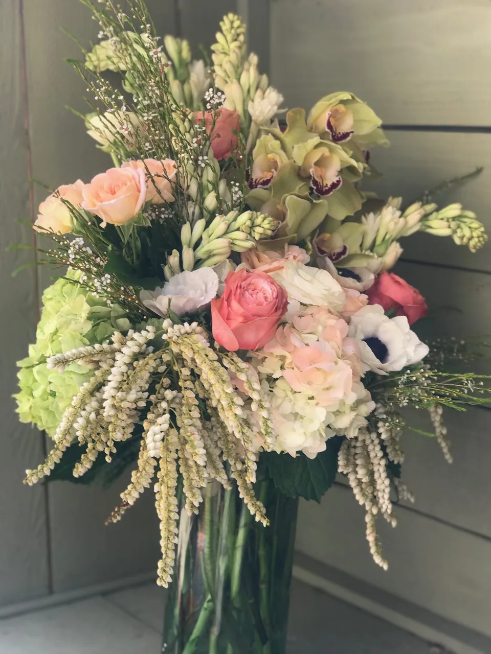 Tall white, blush, and green floral arrangement with trailing white texture and soft pink flowers.
