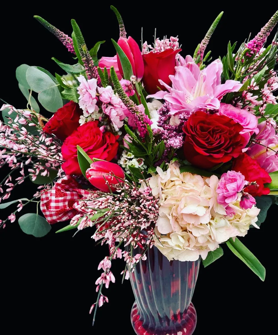 Valentine bouquet with red roses, pale pink flowers, magenta accents, and deep green foliage.