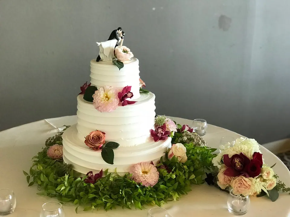 White wedding cake decorated with soft blush flowers and surrounded by floral pieces.